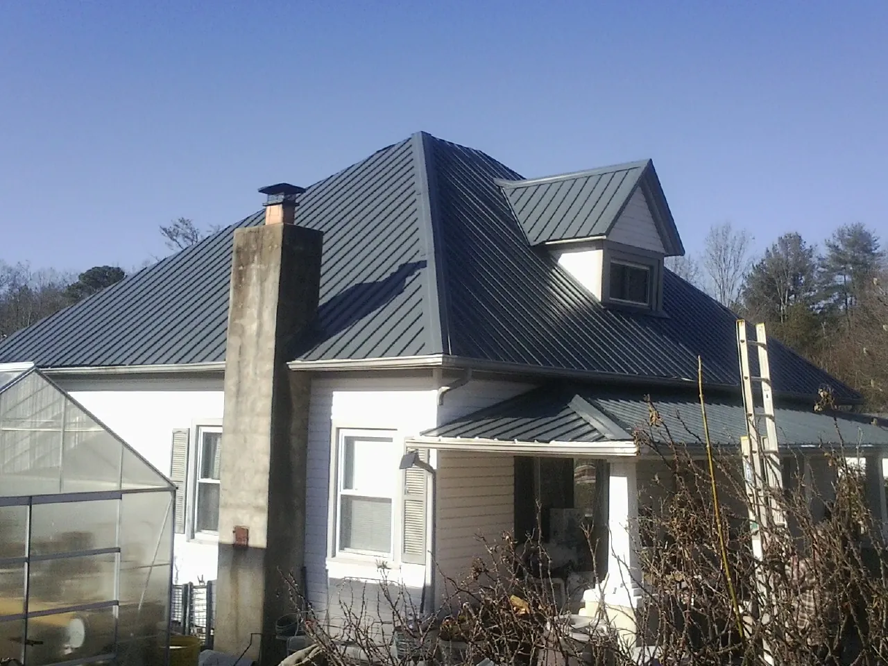 Dark blue standing seam metal roof on a white farmhouse with dormer — Slate & Tile Roof Repair by Roofing Brothers in Roosevelt